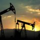 Silhouetted oil pump jacks at sunset in a desert landscape.