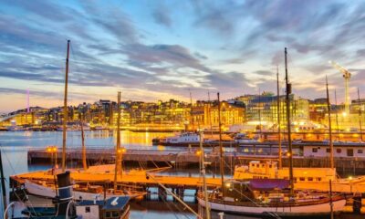 Harbor at dusk with moored sailboats, calm water reflecting warm city lights and a glowing skyline.