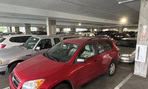 Red compact SUV in a crowded indoor parking garage with concrete pillars and many parked cars around.