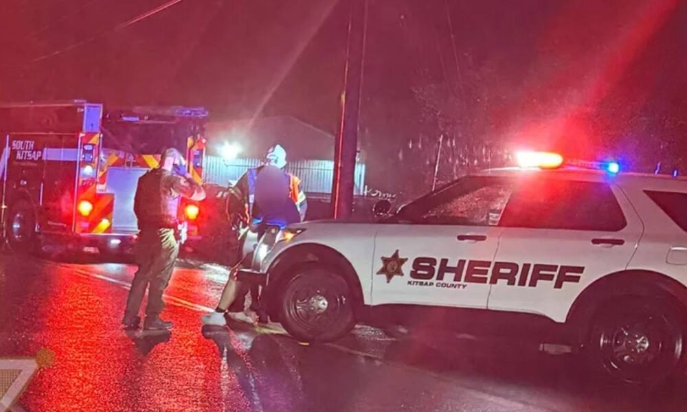 Emergency responders at night on a wet street, sheriff SUV with flashing lights and a fire truck in the background.