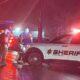 Emergency responders at night on a wet street, sheriff SUV with flashing lights and a fire truck in the background.