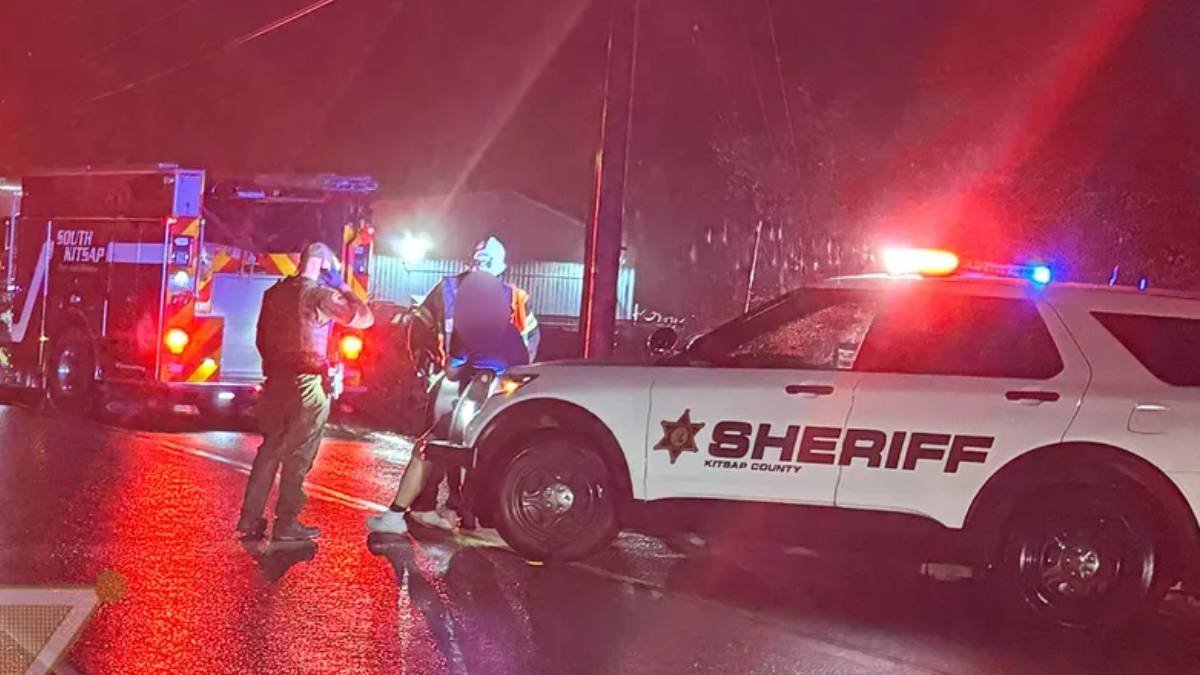 Emergency responders at night on a wet street, sheriff SUV with flashing lights and a fire truck in the background.