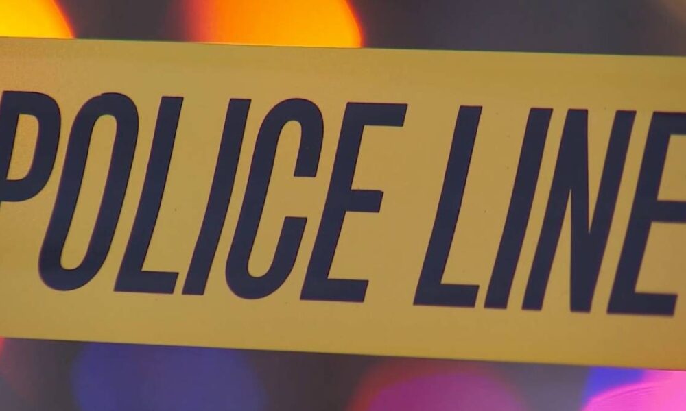 Close-up of yellow police line tape with bold black text POLICE LINE, likely at a crime scene beneath colored lights in the background.