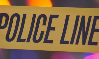 Close-up of yellow police line tape with bold black text POLICE LINE, likely at a crime scene beneath colored lights in the background.