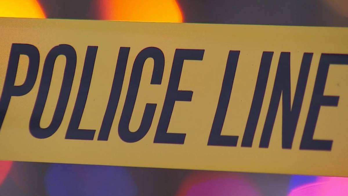 Close-up of yellow police line tape with bold black text POLICE LINE, likely at a crime scene beneath colored lights in the background.