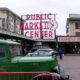 Green vintage truck parked in front of the Public Market Center entrance, with a Farmers Market sign and people walking nearby.