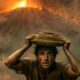 Man wearing a muddy shirt holds a clay pot on his head while chaos and lava glow behind him during an eruption.