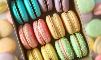 Assorted colorful macarons arranged in a cardboard box, showing teal, pink, yellow, and green hues.