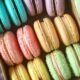 Assorted colorful macarons arranged in a cardboard box, showing teal, pink, yellow, and green hues.