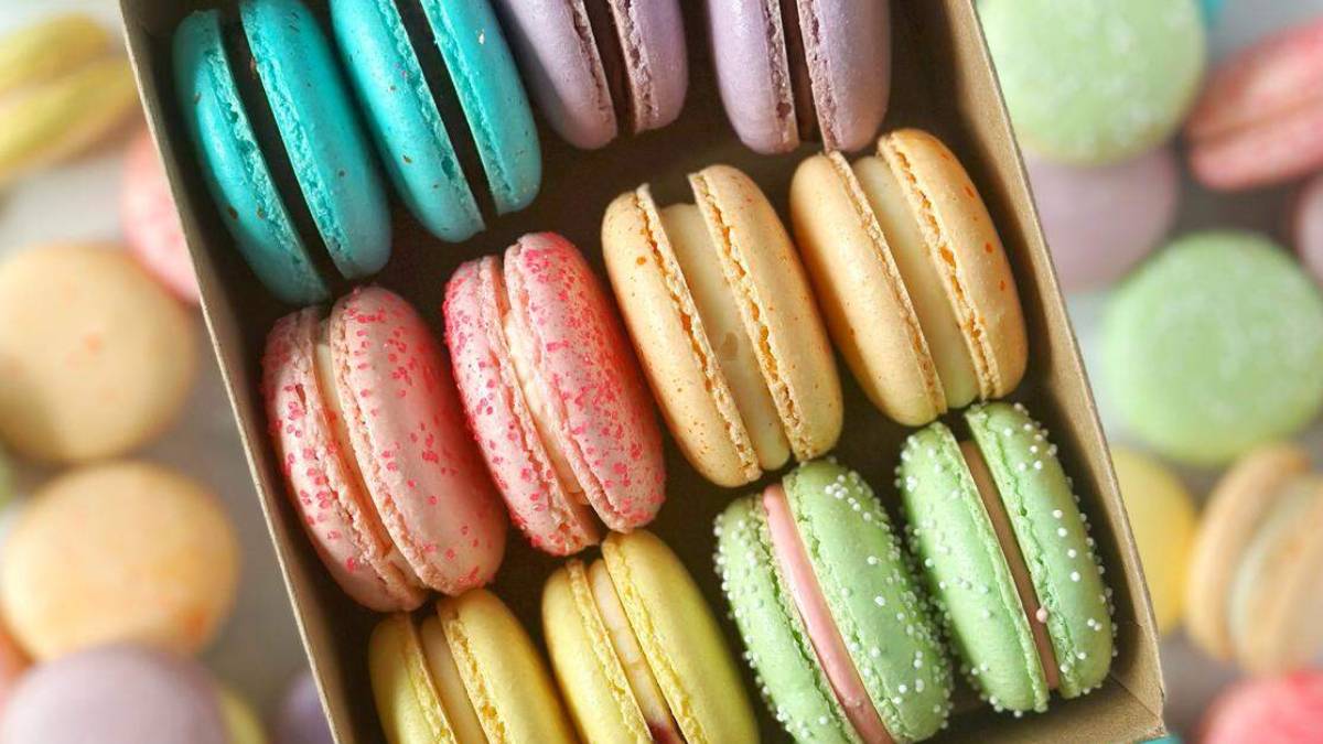 Assorted colorful macarons arranged in a cardboard box, showing teal, pink, yellow, and green hues.