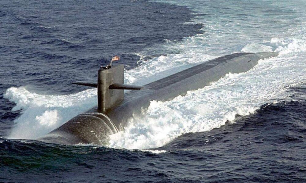 Submarine surfacing in choppy seas, with the sail and conning tower visible above water and a periscope extending upward.