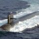 Submarine surfacing in choppy seas, with the sail and conning tower visible above water and a periscope extending upward.