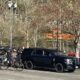 Two police officers stand near a dark SUV marked Police, beside a trailer with a solar panel in a parking lot near train tracks.