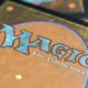 Close-up of a Magic: The Gathering card back with an orange-brown field and a blue, stylized 'MAGIC: The Gathering' logo.