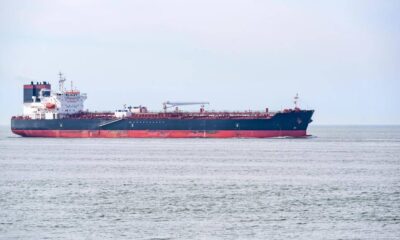 Large blue-and-red tanker sailing on a calm sea with a distant horizon in the background, white superstructure toward the aft.