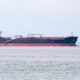 Large blue-and-red tanker sailing on a calm sea with a distant horizon in the background, white superstructure toward the aft.