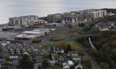 Aerial view of a coastal town with apartment buildings along the shoreline, a shopping plaza, and winding roads.