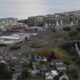 Aerial view of a coastal town with apartment buildings along the shoreline, a shopping plaza, and winding roads.