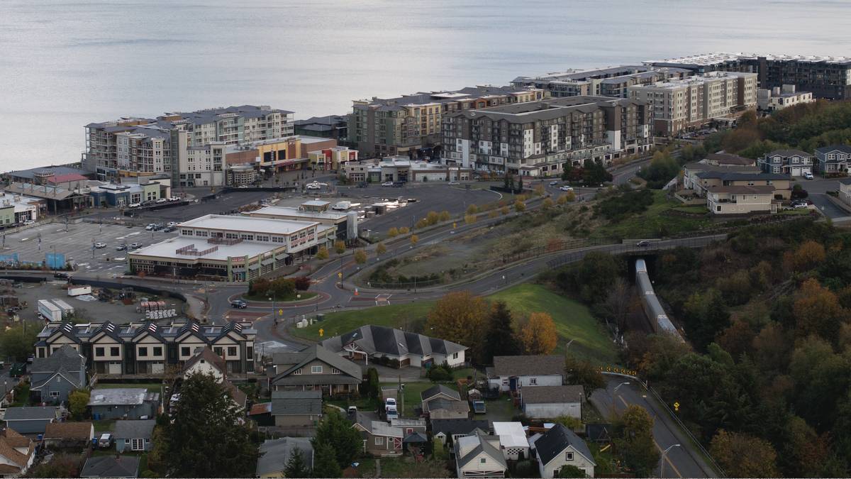 Aerial view of a coastal town with apartment buildings along the shoreline, a shopping plaza, and winding roads.
