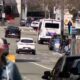 Busy city street with cars and a white bus, blurred cyclist in foreground on a sunny day.