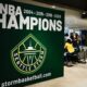 Large green banner reading 'WNBA CHAMPIONS' with years and the Seattle Storm logo, plus stormbasketball.com, in an indoor event space with people nearby.