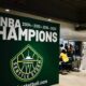 Large green banner reading 'WNBA CHAMPIONS' with Seattle Storm logo, celebrating championships (2004–2010–2018–2020). Inside venue with people nearby.