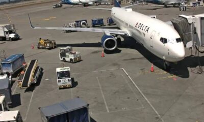 Delta Air Lines passenger jet docked at gate with jet bridge connected and ground support vehicles around it on the tarmac