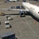 Delta Air Lines passenger jet docked at gate with jet bridge connected and ground support vehicles around it on the tarmac