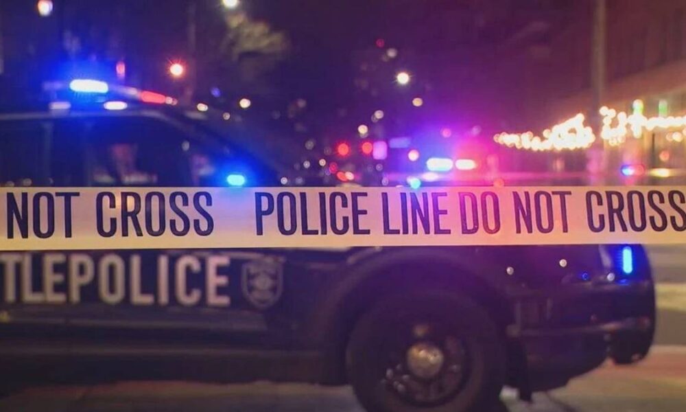 Police car with flashing blue and red lights behind 'Do Not Cross' tape at night, creating a crime scene scene.