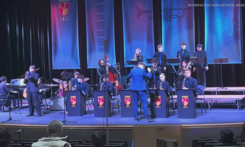 Shorewood High School Jazz Band performs on stage with a conductor directing the players and banners in blue backdrop.