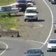 Small white and blue single-engine plane on a grassy verge beside a busy highway with cars passing by.