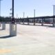 Empty parking lot with concrete dividers, tall light posts, and a long covered roadway in the distance under a clear blue sky.