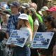 Group of diverse protesters at a rally, holding signs that say 'Save Rail to Ballard' and 'Do not stop short!'