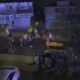 Group of people walking along a residential street at night, with houses and string lights visible in the background.