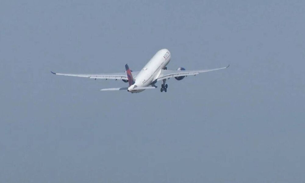 A white commercial airliner lifting off with landing gear down, engines roaring, against a pale blue sky.