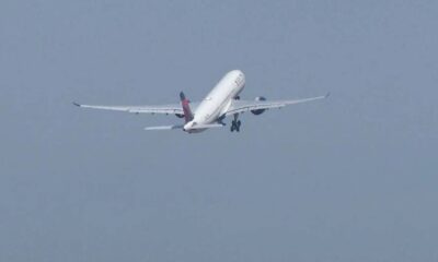 A white commercial airliner lifting off with landing gear down, engines roaring, against a pale blue sky.