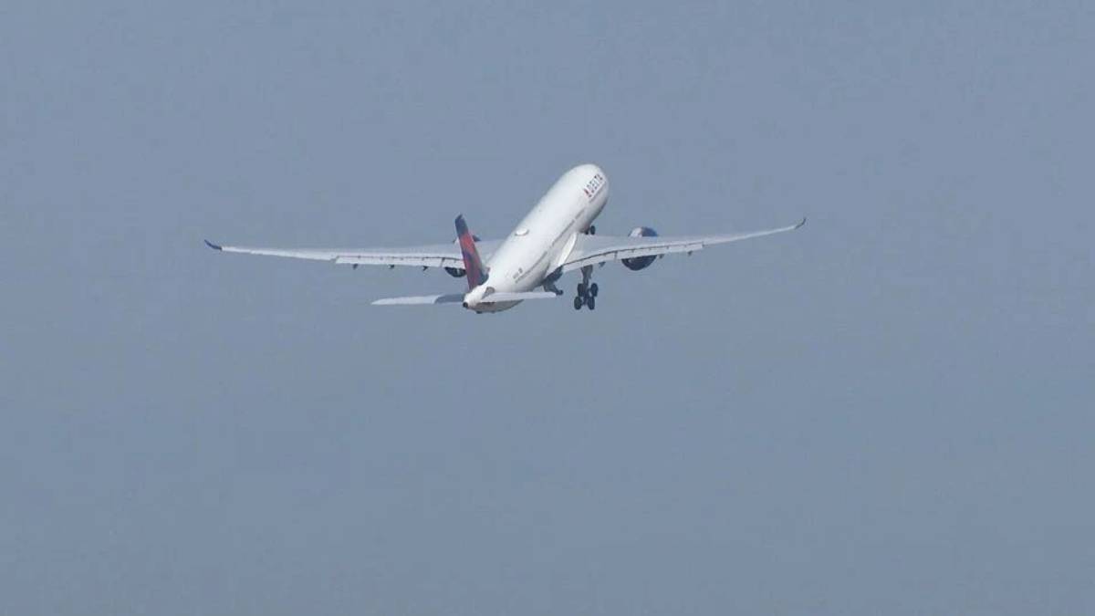 A white commercial airliner lifting off with landing gear down, engines roaring, against a pale blue sky.