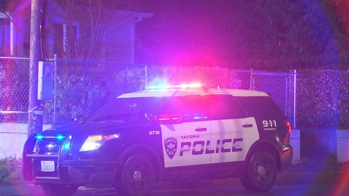 Tacoma Police Department SUV with red and blue emergency lights flashing at night beside a chain-link fence.
