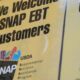 Sign reads 'We Welcome SNAP EBT Customers' with a small USDA SNAP logo on a yellow background (close-up).