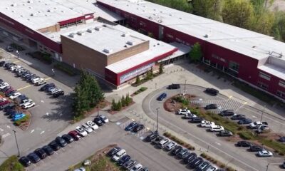 Aerial view of a large red-brick school building with a white roof, surrounded by parking lots and a circular driveway with cars and landscaped medians.