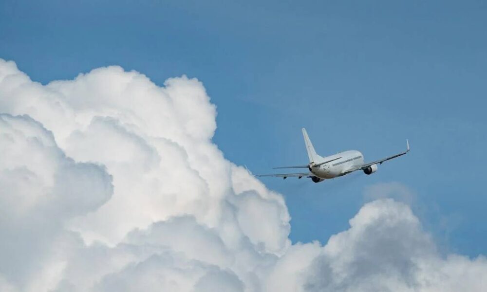 Commercial airliner flying through a blue sky with large white clouds nearby.