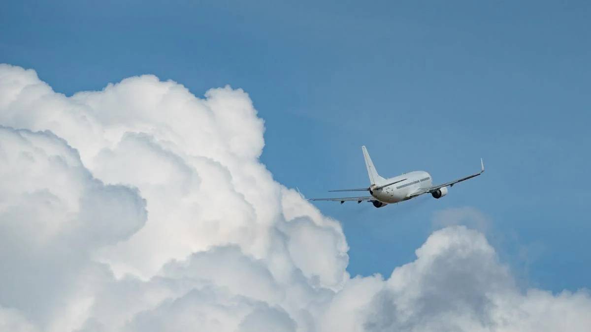 Commercial airliner flying through a blue sky with large white clouds nearby.