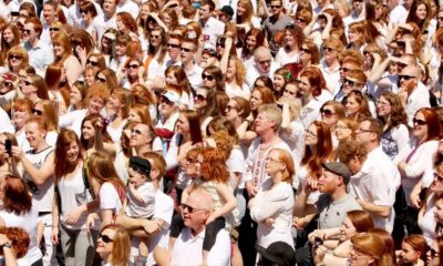 Large crowd of people wearing white shirts gathered outdoors, looking toward something off-camera.