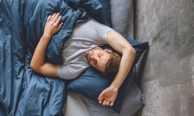 Man sleeping on his side in bed with dark blue sheets and gray pillow. (informative)
