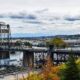 Steel lift bridge over a harbor with boats, cityscape in distance and autumn trees in the foreground.