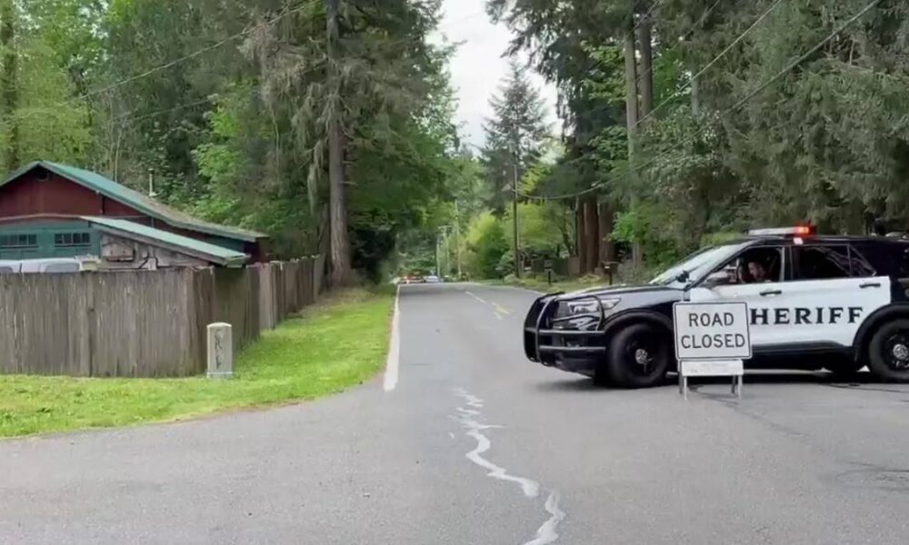 Sheriff SUV blocking a quiet residential road with a 'Road Closed' sign in the foreground and trees lining the street.