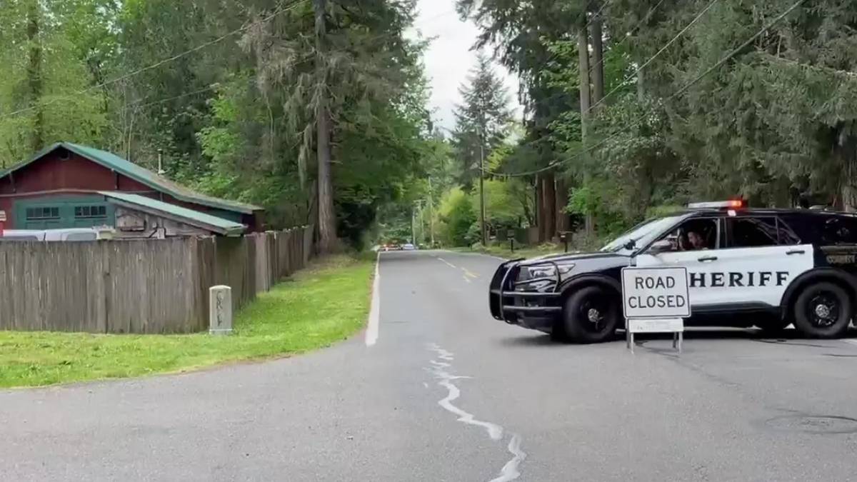 Sheriff SUV blocking a quiet residential road with a 'Road Closed' sign in the foreground and trees lining the street.