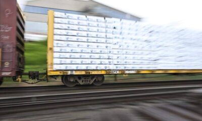 Blurry cargo train car on a flatbed carrying stacked white-wrapped pallets, in motion.