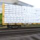 Blurry cargo train car on a flatbed carrying stacked white-wrapped pallets, in motion.