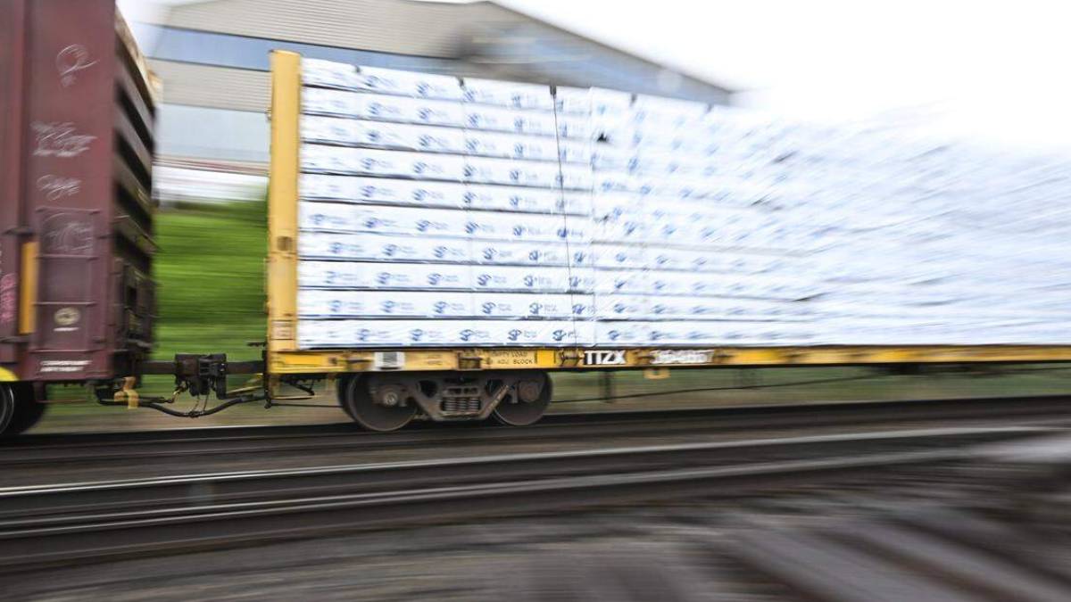 Blurry cargo train car on a flatbed carrying stacked white-wrapped pallets, in motion.